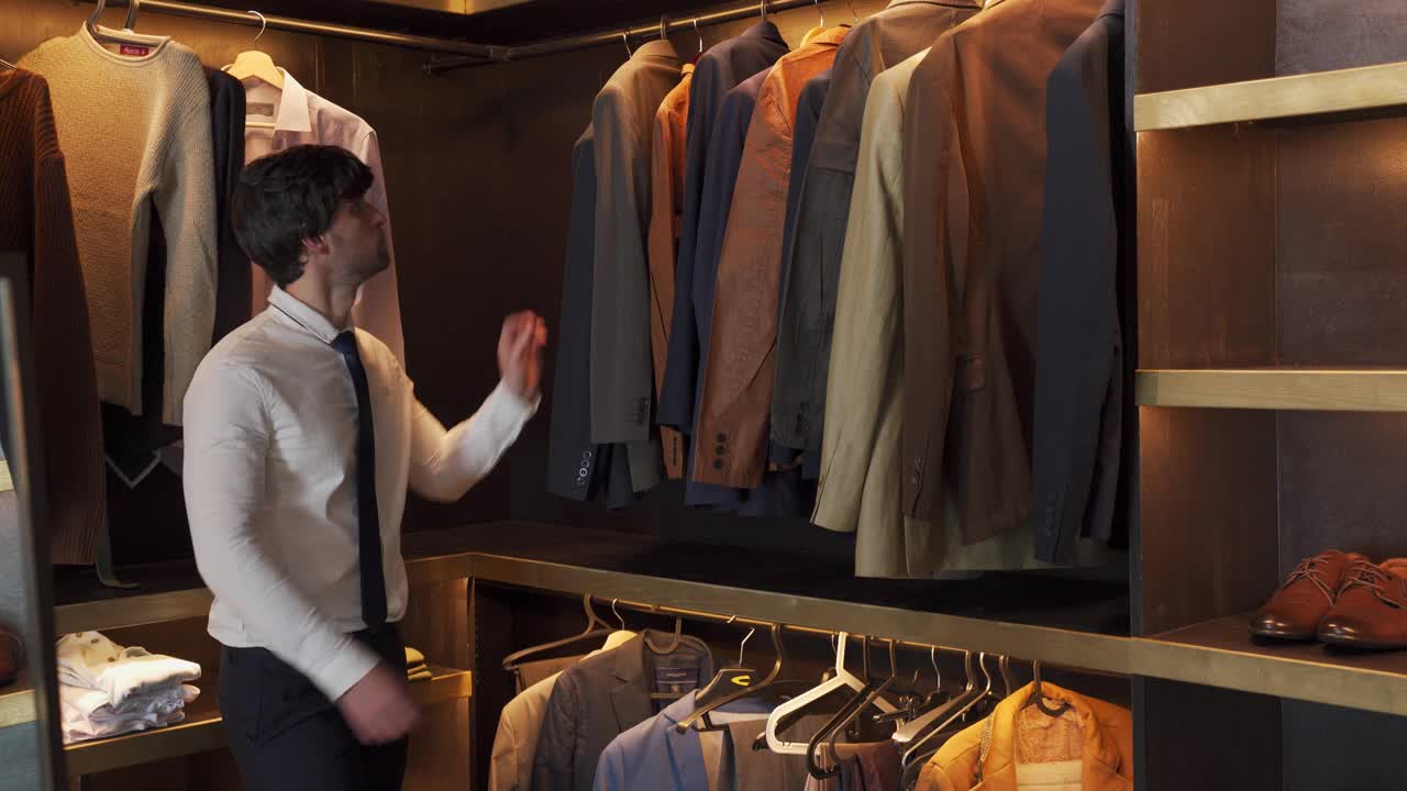 一名男子在服装店挑选一件挂在衣架上的西装外套视频下载