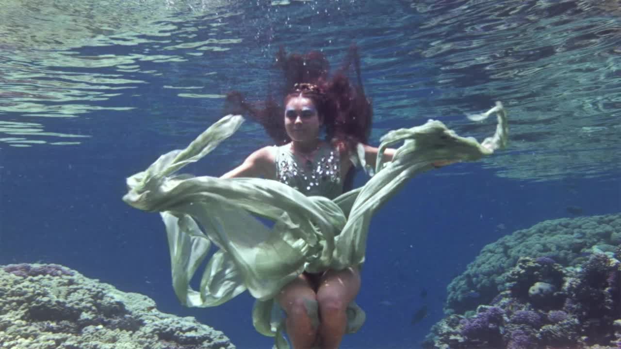 年轻的女孩在红海的珊瑚背景下水下为相机摆姿势。视频下载
