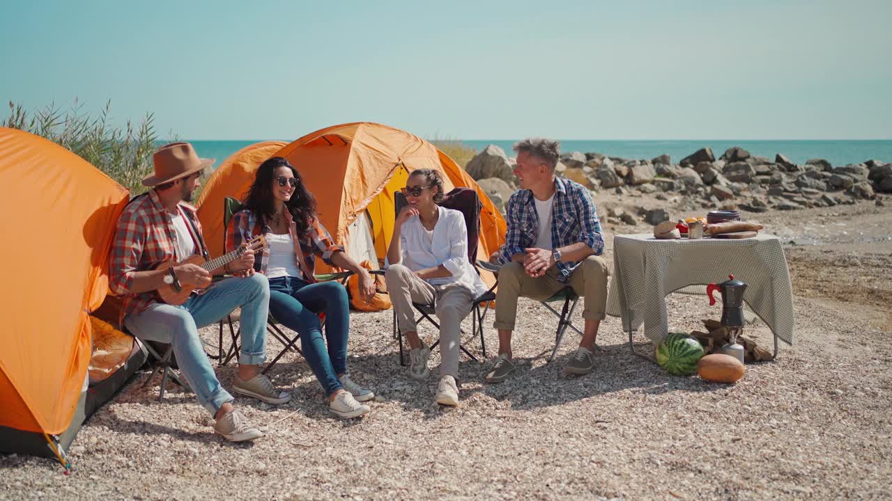 野餐的年轻人和尤克里里琴在海滩上与帐篷视频下载
