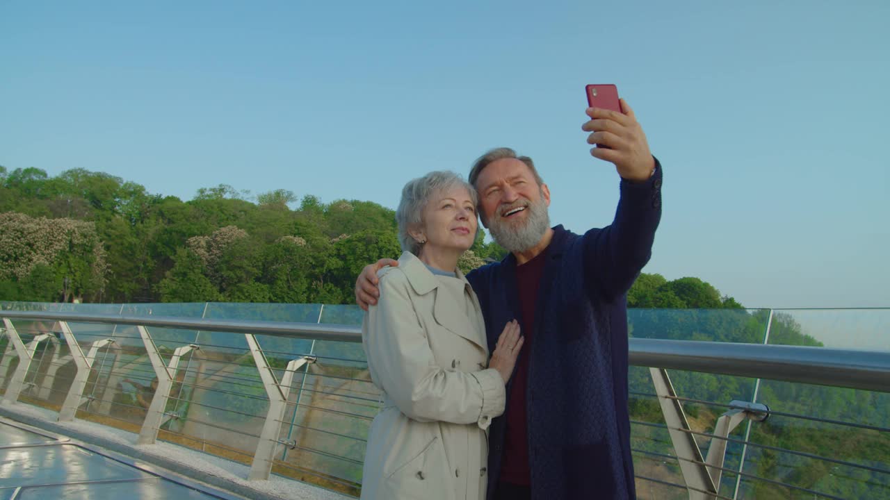 微笑的老人拿着智能手机和他的配偶自拍视频下载