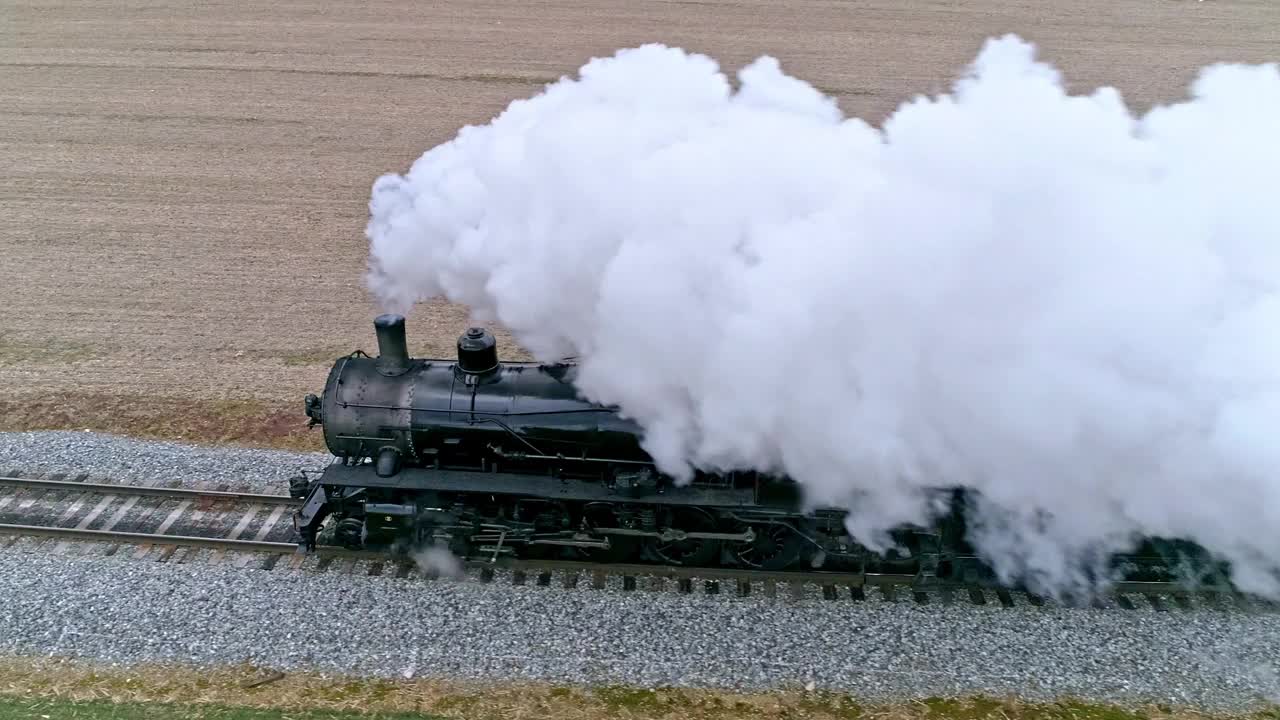 空中近距离观看蒸汽火车与无人机沿着一边吹烟和蒸汽旅行的乡村在一个冬天的一天视频下载