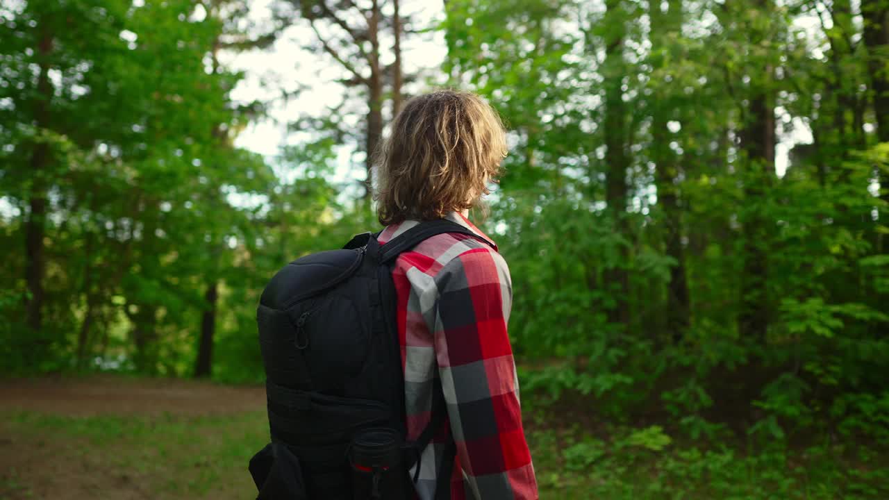 一个背着背包戴着墨镜的男人在树林里。弧开枪。视频下载