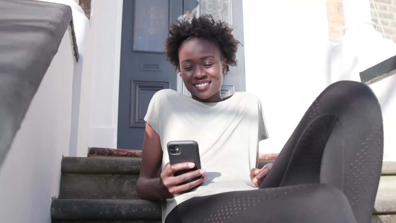 年轻女性坐在外面阳光下查看手机视频下载
