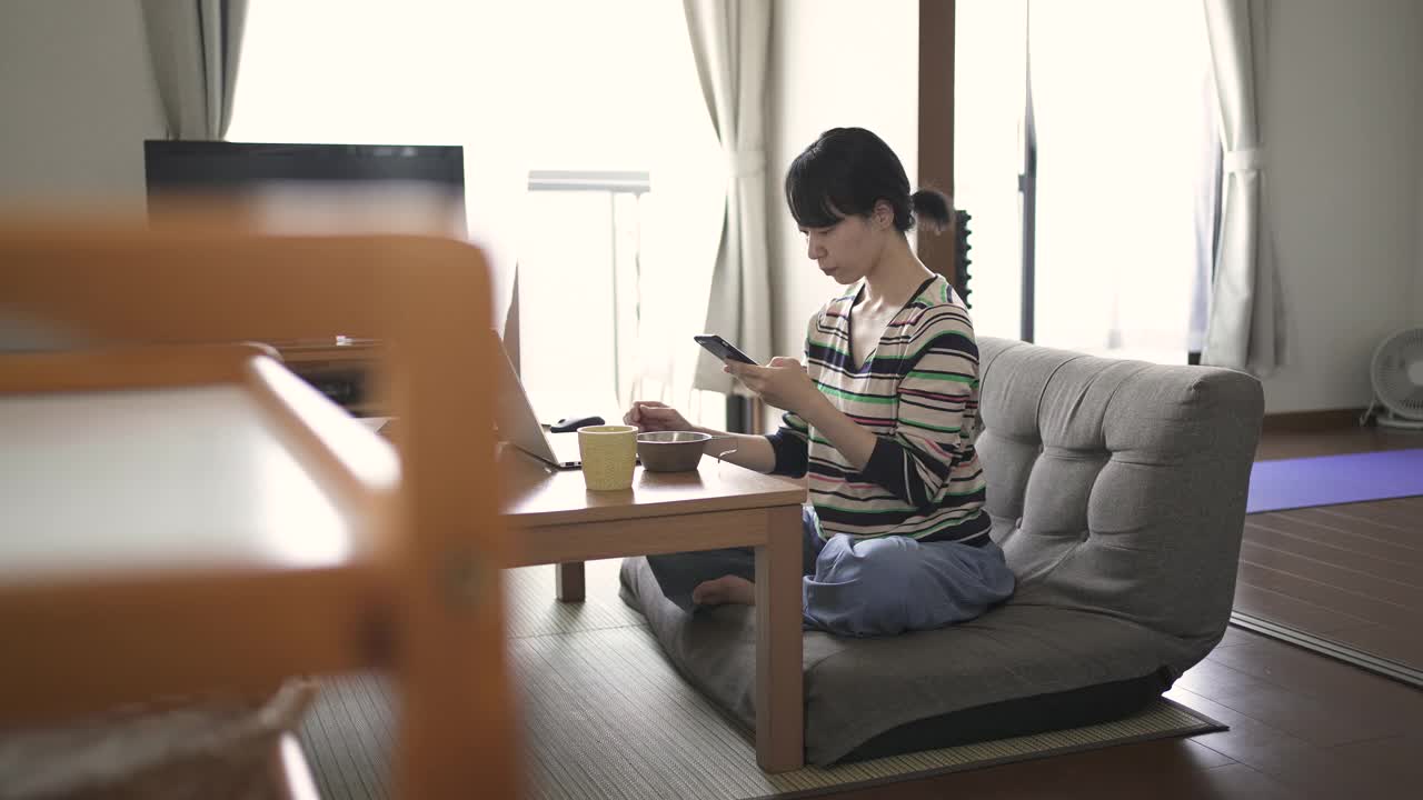 在家工作，在客厅使用电脑和智能手机的中年妇女。视频下载