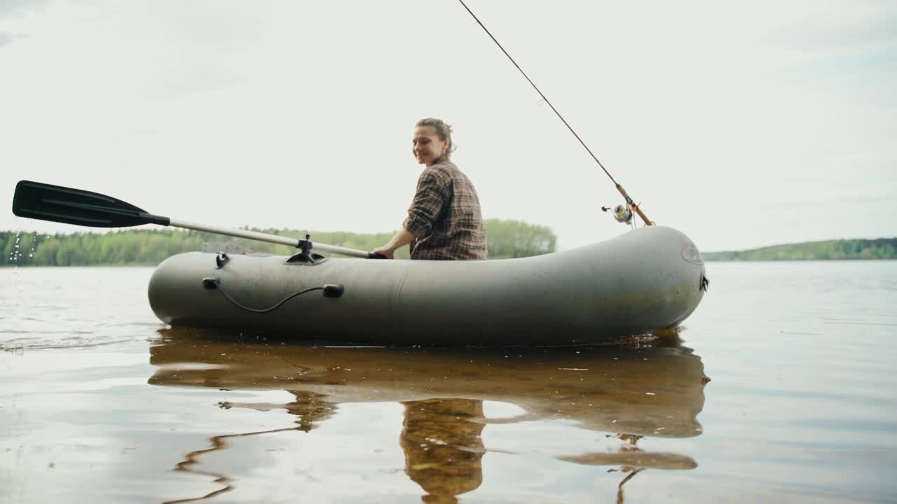 年轻的渔夫在湖上的一只充气船上划桨。视频下载