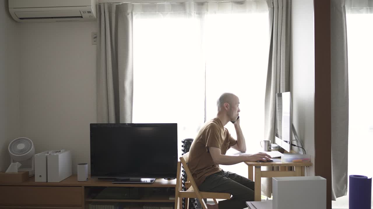 中年人在家工作，看着电脑屏幕，给客户打电话。视频下载
