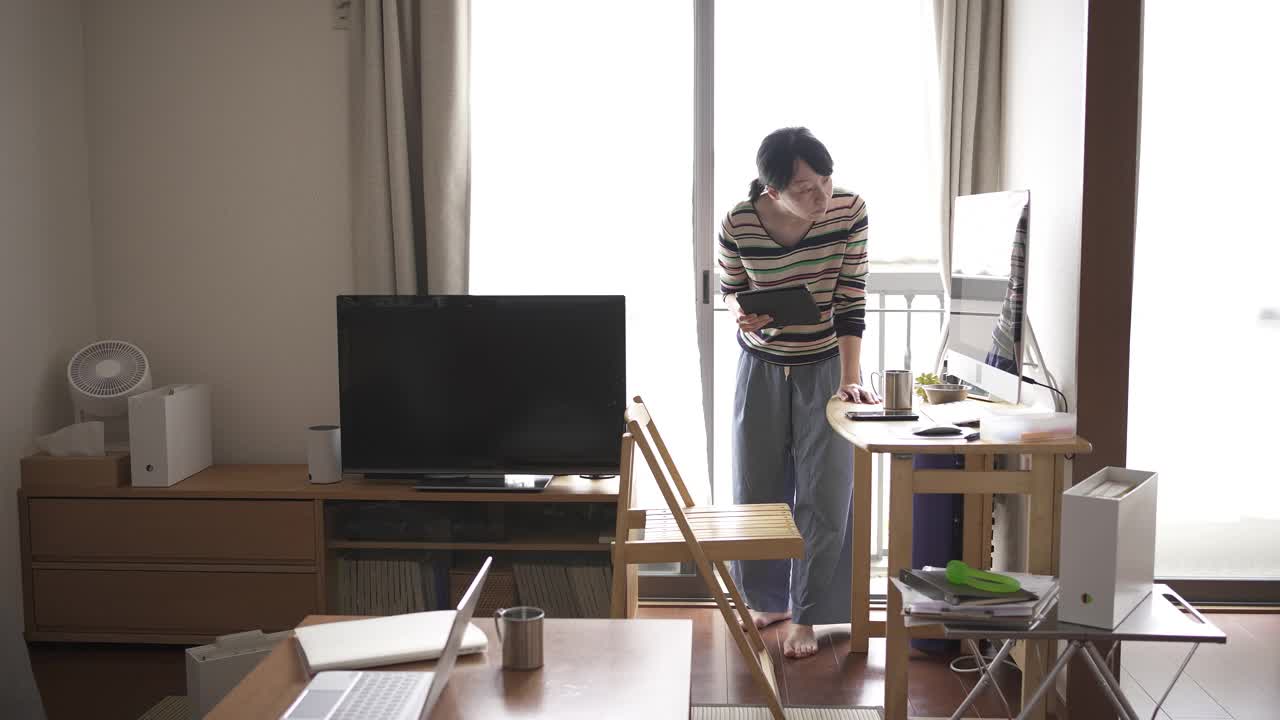 中年妇女在家工作，用着窗边的平板电脑。视频下载