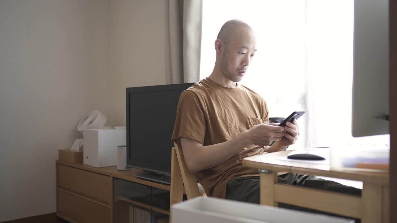 中年男性在家工作，在客厅使用电脑和智能手机。视频下载