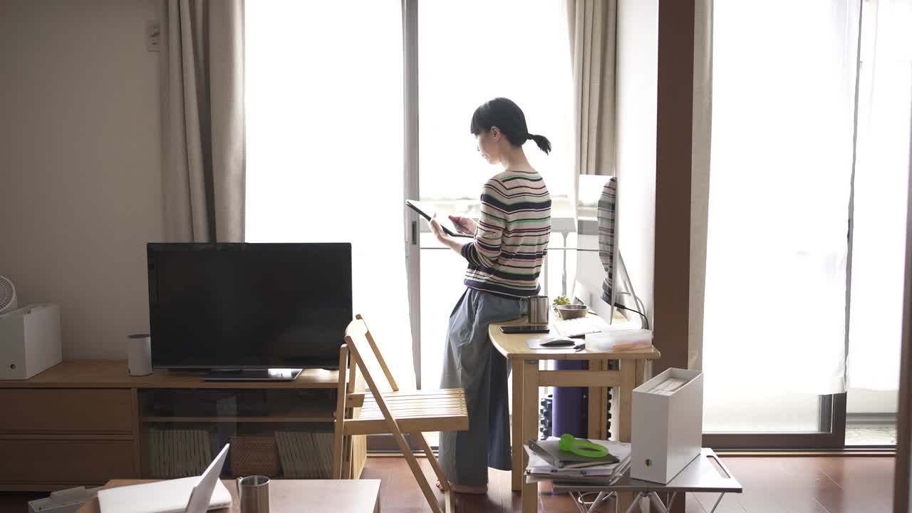 中年妇女在家工作，用着窗边的平板电脑。视频下载