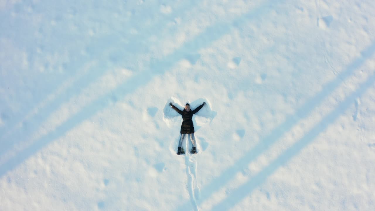 一个年轻漂亮的女人描绘了一个雪天使躺在新雪上。一个充满活力和快乐的女人在新鲜寒冷的空气中玩雪。视频下载