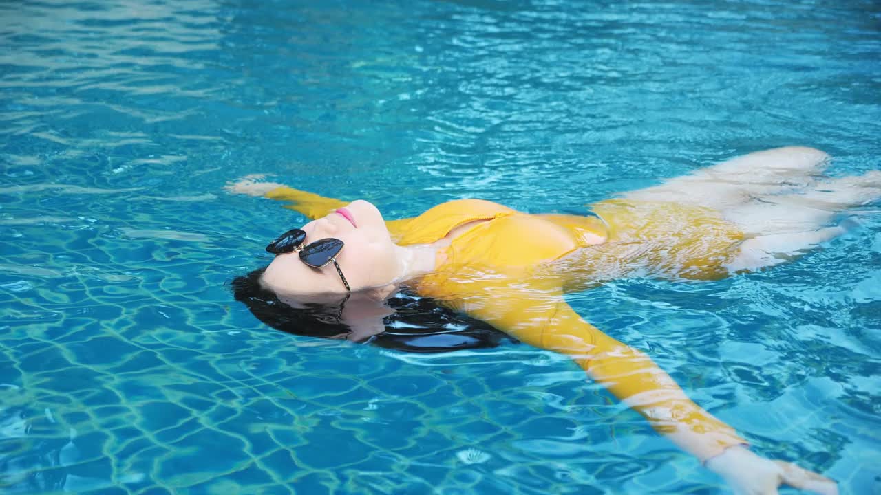 亚洲女子放松在黄色游泳仰泳在度假胜地冷却。视频下载