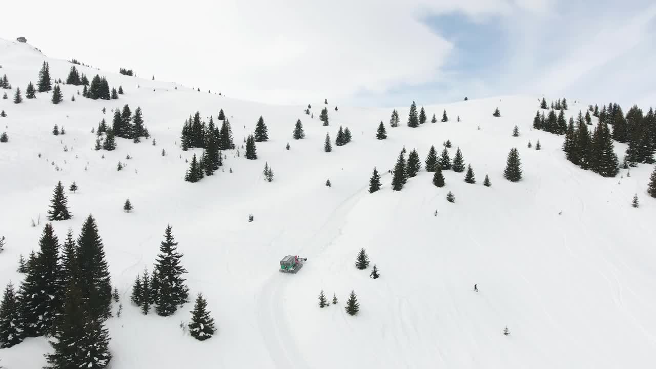 雪地车在雪道外的滑雪场斜坡上行驶，登上积雪覆盖的山顶，发生事故和滑雪者受伤的紧急情况。鸟瞰图视频下载