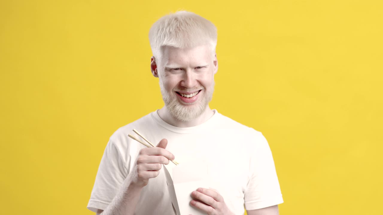 白化病的家伙吃面条享受垃圾食品在黄色的背景视频下载