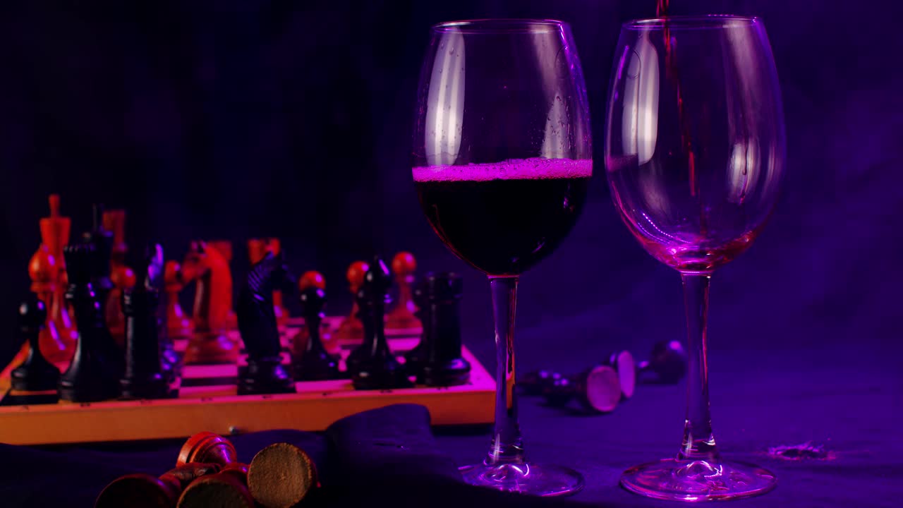 近距离的两个葡萄酒杯在黑色背景与照明和消散的蒸汽。一个不认识的人把红酒倒进第二个杯子里视频下载