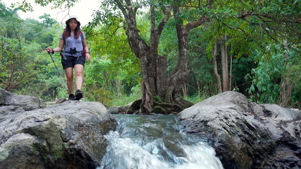 亚洲女子站在岩石上属于瀑布的放松，独自在热带森林中穿越蒸汽带着危险的感觉，再次启程前，年轻女子喜欢冒险之旅视频素材