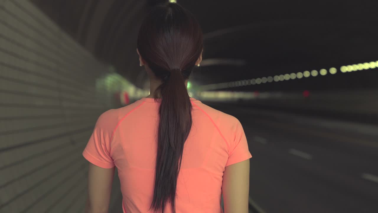 运动和锻炼——在韩国城市的隧道里，年轻女子一边走一边看智能手表的背影视频下载