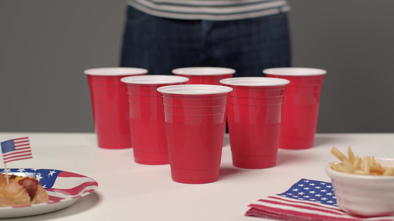 在啤酒乒乓游戏中，当背景中的人在喝酒时，滑动射击接近杯子视频下载