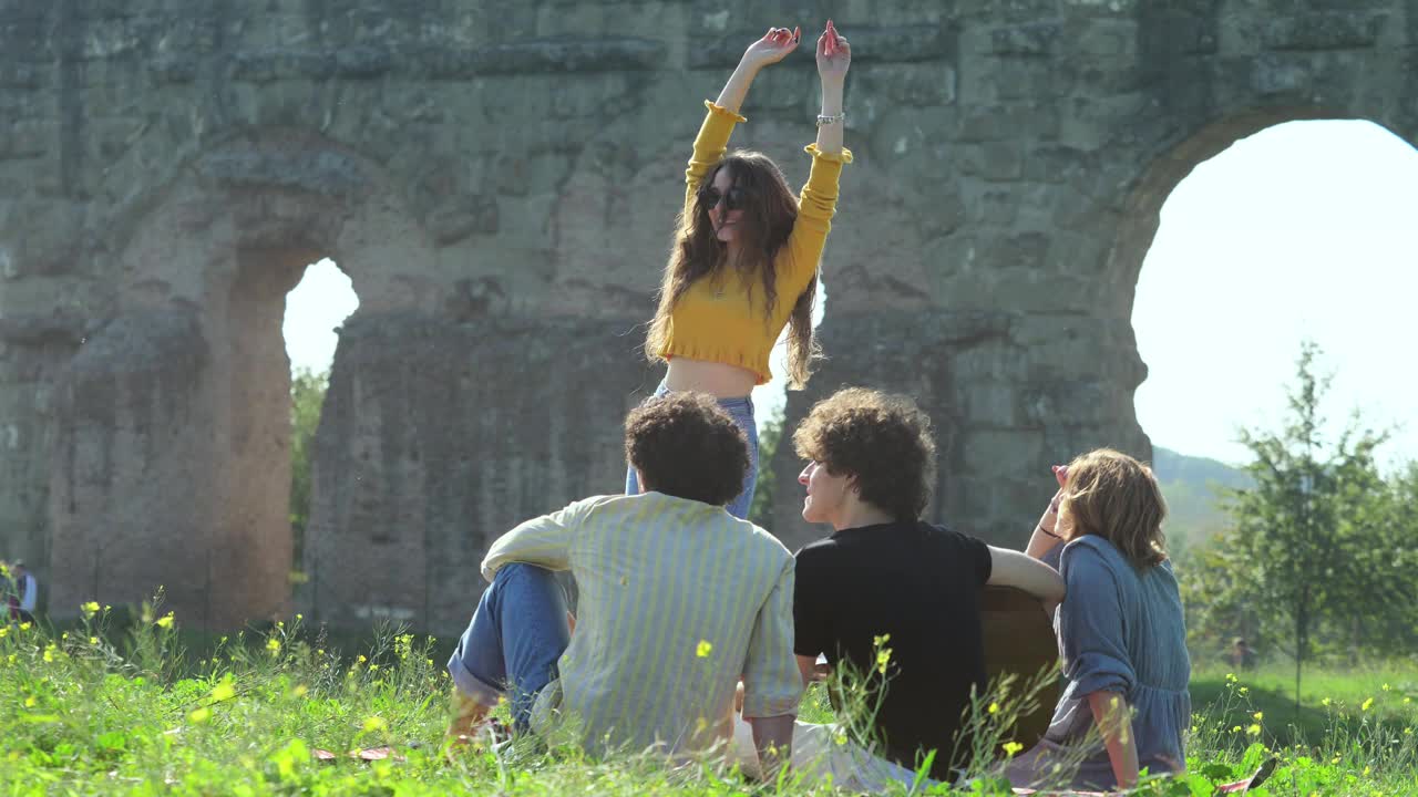 快乐的女孩在公园里和她的朋友们坐在草地上跳舞唱歌视频下载