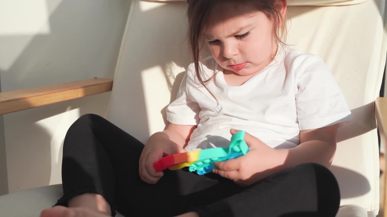 蹒跚学步的小女孩和彩虹色的popit玩具。恐龙形状的硅树脂玩具的压力救济。泡泡感觉时髦的烦躁。孩子在家里率直地玩耍视频下载