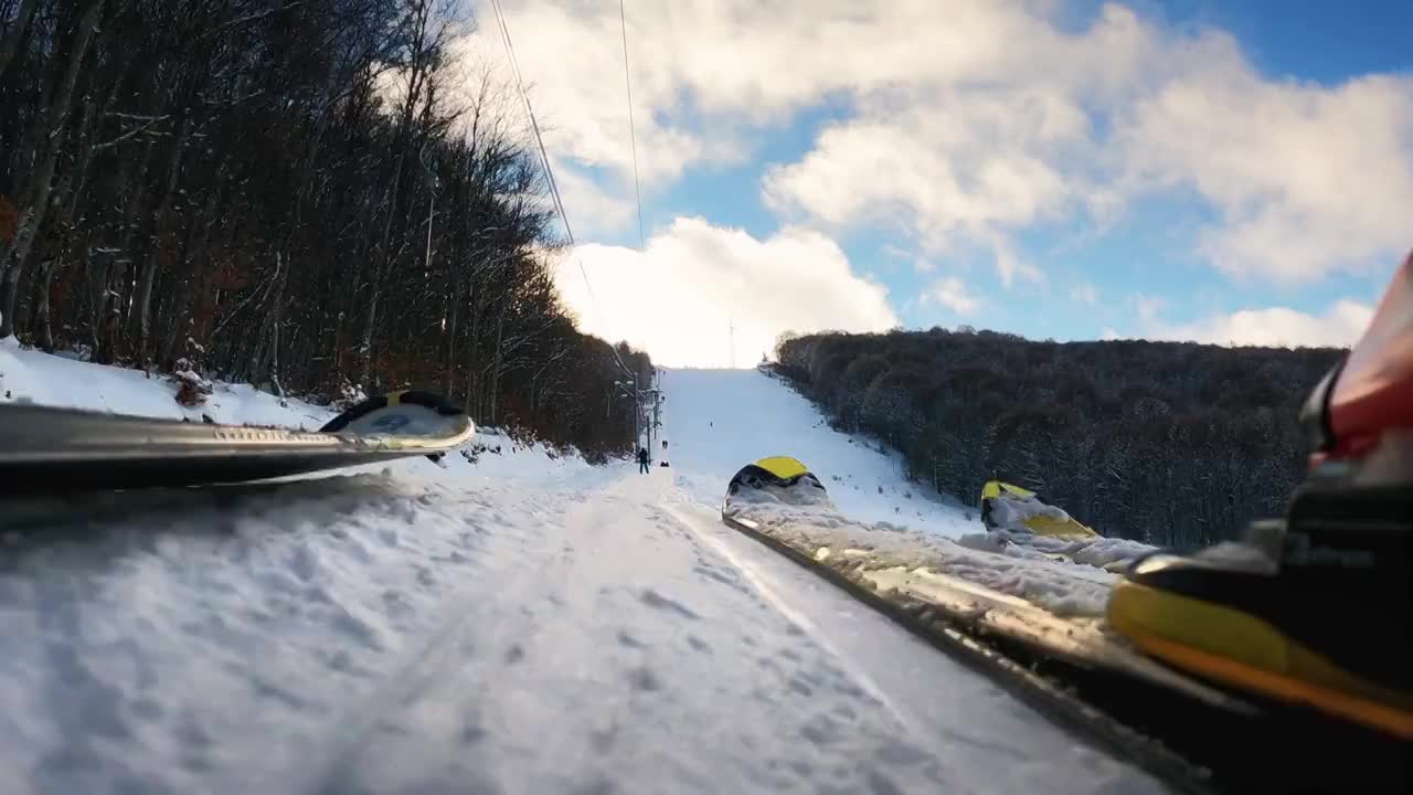 在一个阳光明媚的冬日，一对夫妇的滑雪板在t杆(拖)滑雪缆车上上坡。慢动作视频购买