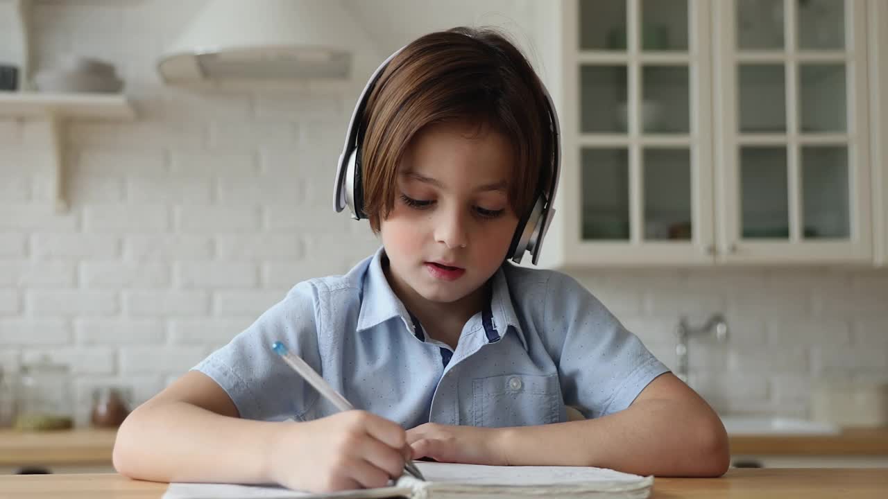 漂亮的小男孩戴着耳机与在线导师交流视频下载