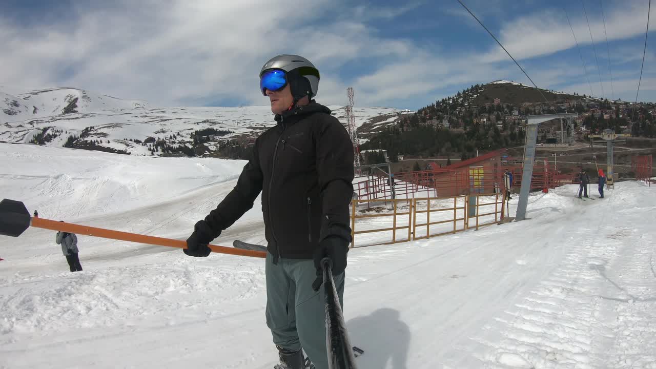 快乐的年轻男性滑雪者使用滑雪拖曳升降机和问候挥舞他的滑雪杆视频下载