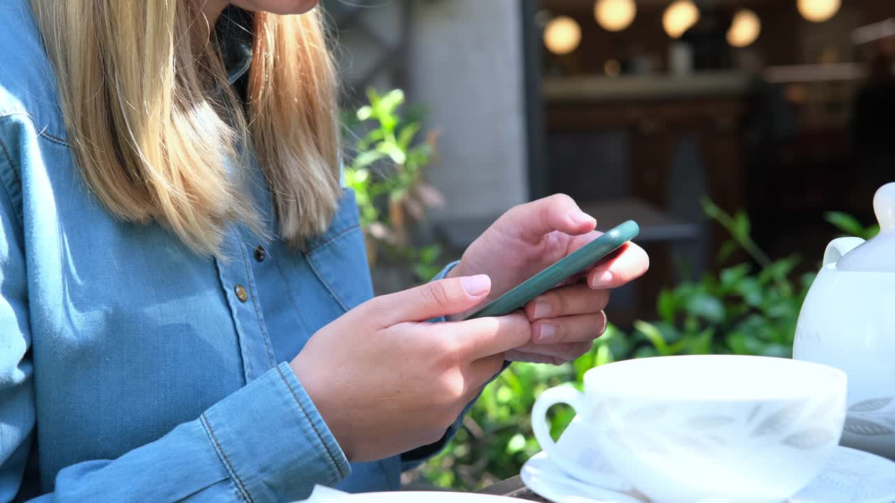 一位年轻女子的手触碰着智能手机的屏幕。年轻的金发女人在她的智能手机上写信息或网上购物视频素材