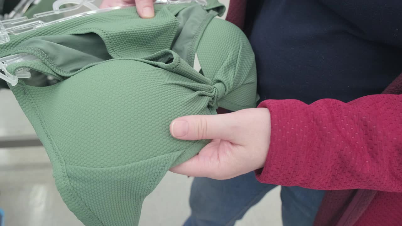 孕妇在商店里选择一件浅绿色的泳衣。双手特写视频下载
