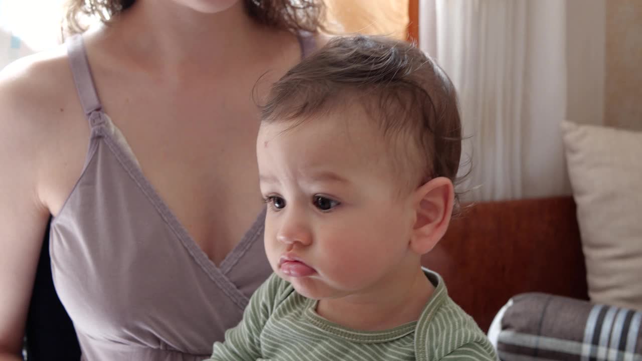 婴儿坐在妈妈的怀里时，妈妈给他梳头发视频下载