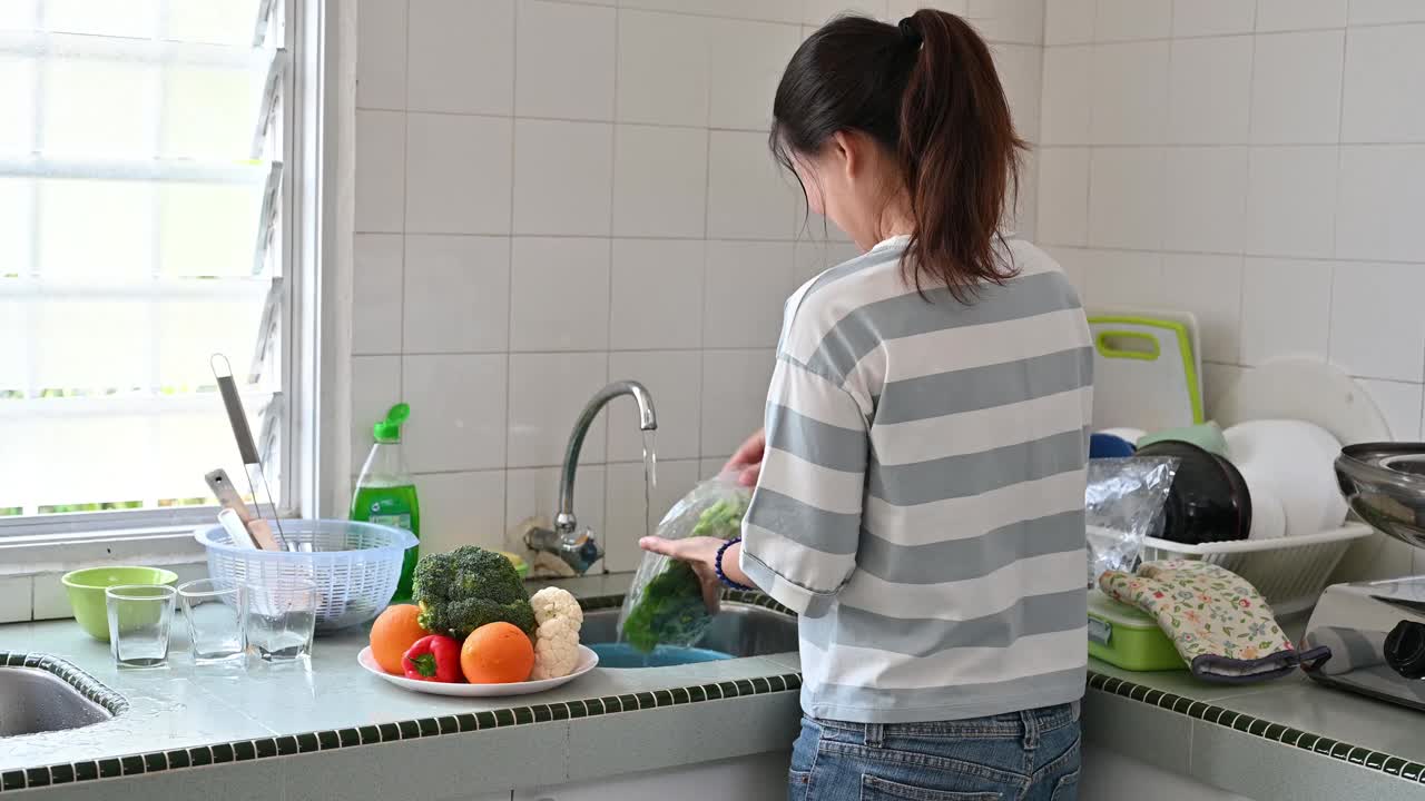 一位亚洲妇女在厨房用手清洗新鲜蔬菜花椰菜视频下载