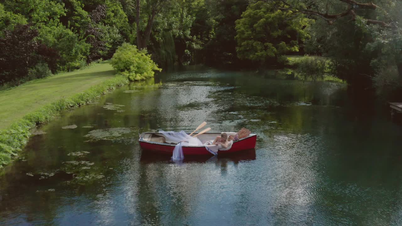 一个美丽性感的女人放松与绿色的树在划船的背景-无人机拍摄视频下载