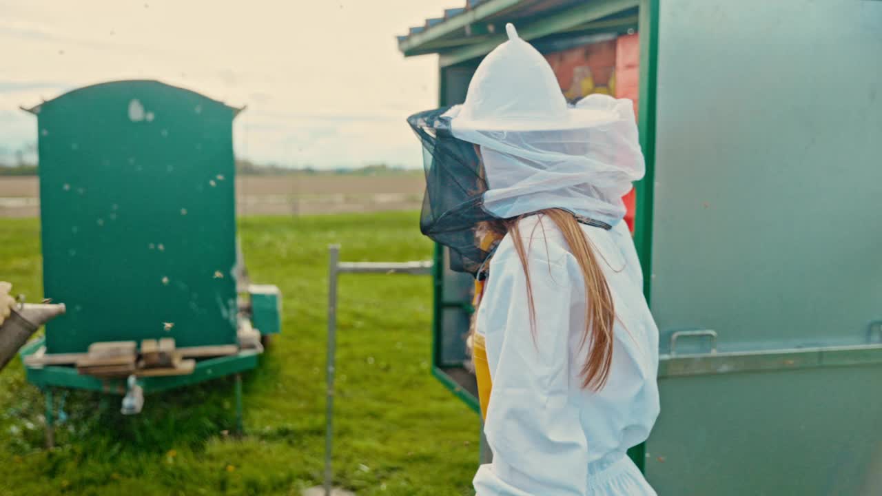 养蜂人穿着防护服，在蜂箱前放着飞行的蜜蜂视频下载