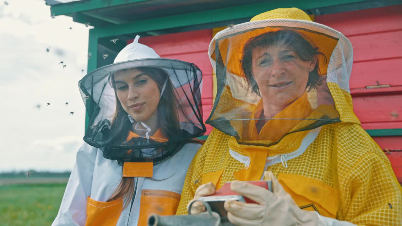 雌性养蜂人穿着保护性的工作服，与飞舞的蜜蜂一起站在蜂箱前视频下载