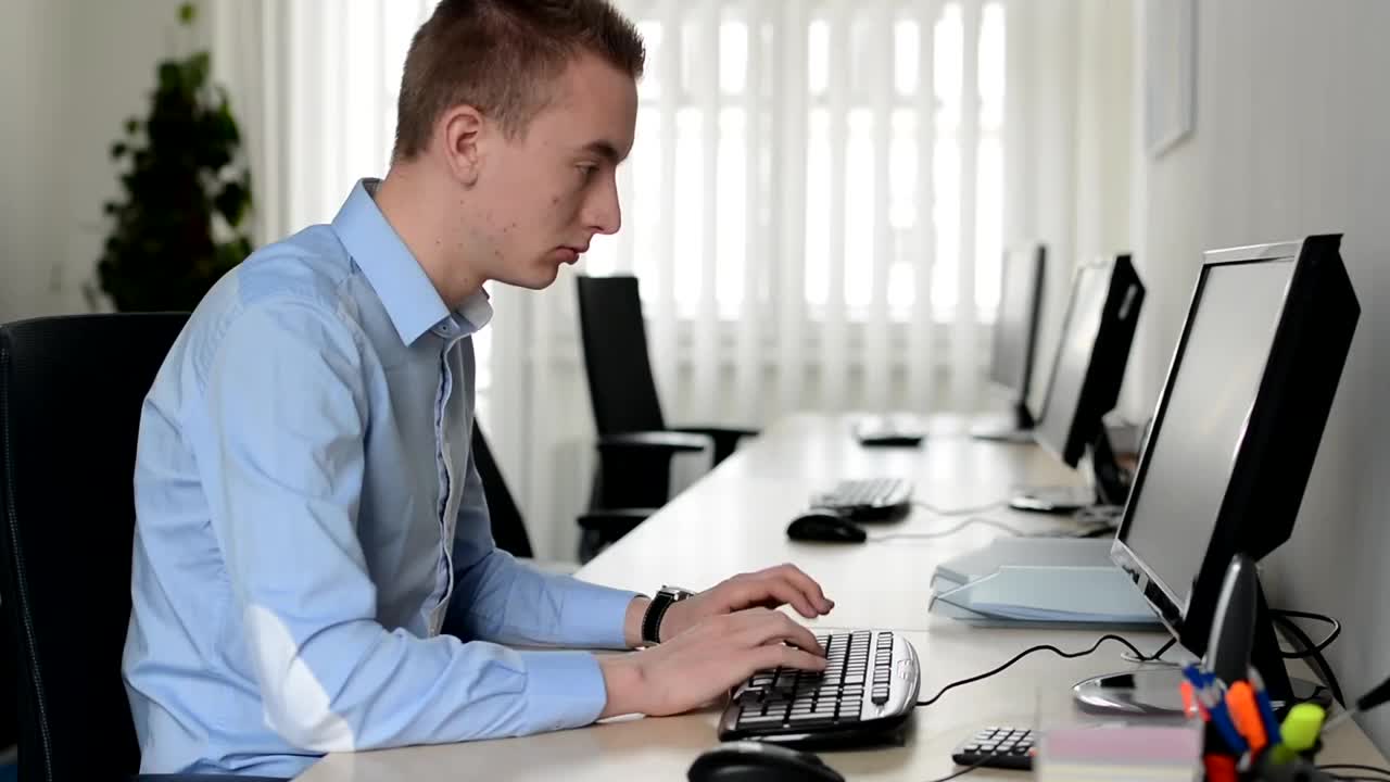 年轻英俊的男子坐在办公室的电脑里，对着摄像机微笑着工作视频素材