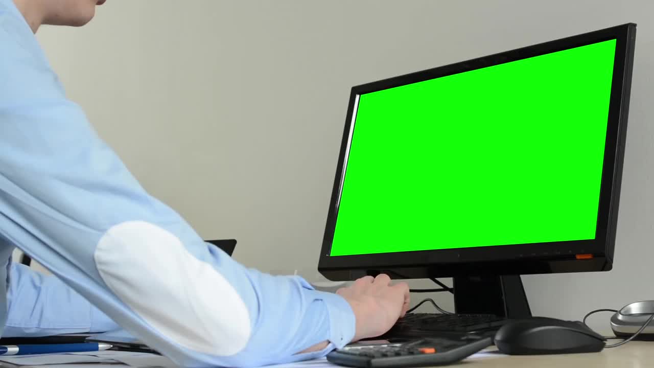 年轻英俊的男子坐在办公室的台式电脑上工作-绿色屏幕-特写视频素材