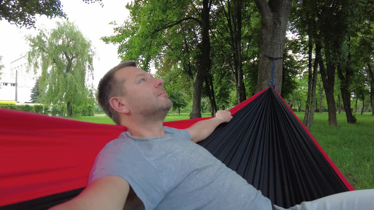 公园里的那个人正在吊床上荡来荡去，享受夏天。视频下载
