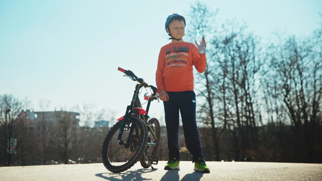 男孩戴着自行车头盔，从瓶子里喝水视频素材
