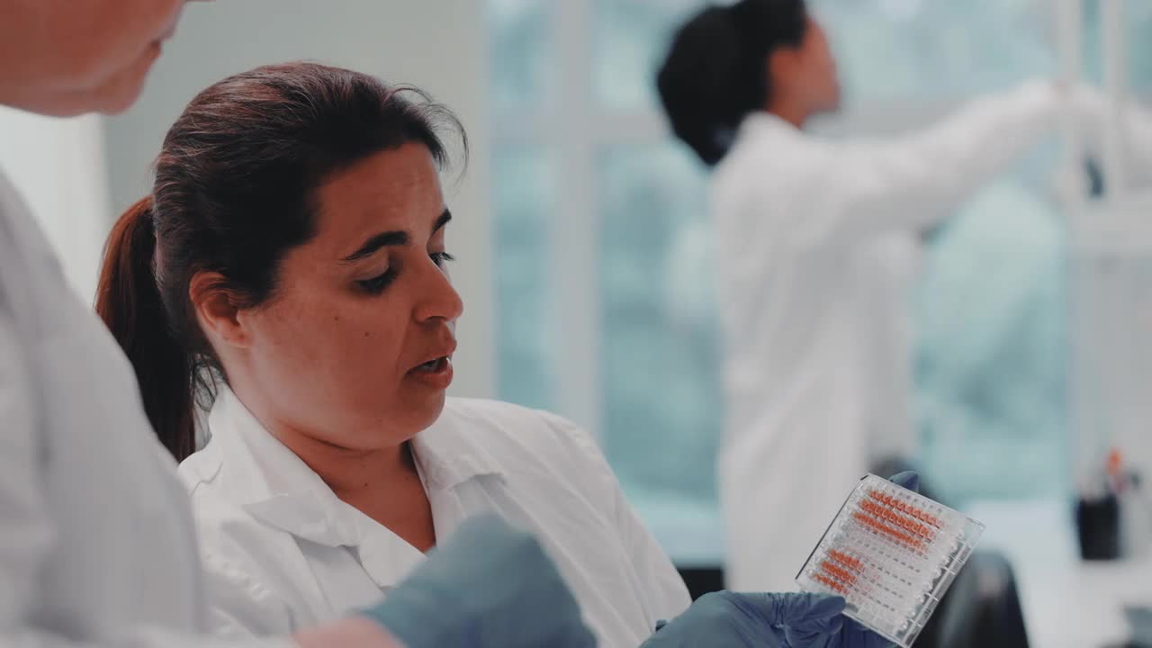 成熟的女科学家在实验室与同事讨论微孔板视频素材