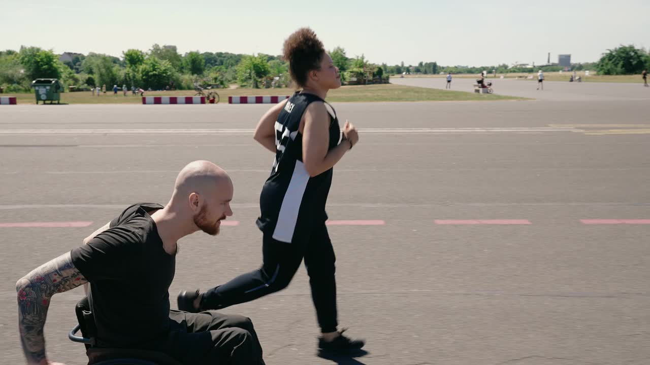 一个女人和一个坐轮椅的男人在旧机场跑道上慢跑视频素材