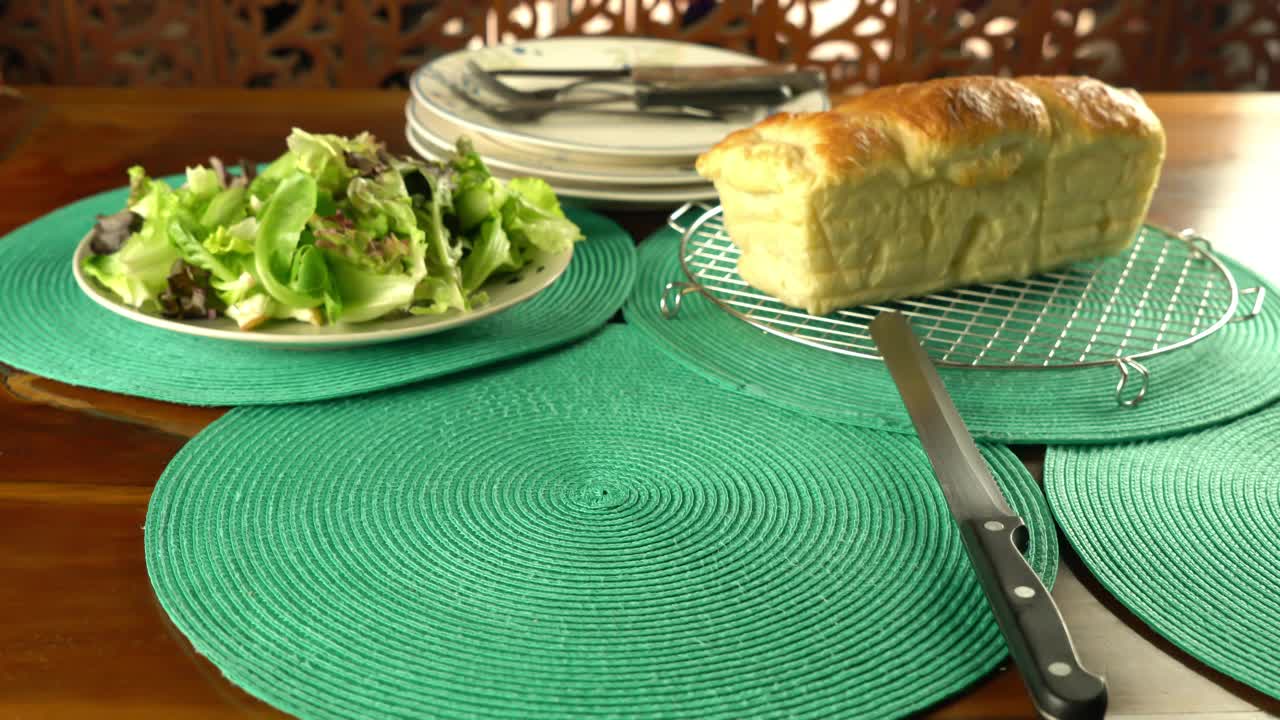 年长的男侍者把一碟白色陶瓷火腿芝士乳蛋饼放在蓝色的桌布上，还有一盘各种蔬菜，一条刚烤好的面包放在金属冷却架上。视频下载