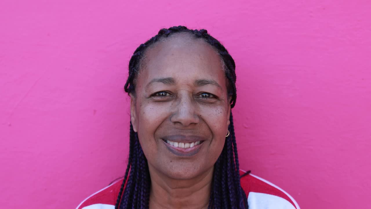一位非洲年长女性微笑着，用粉红色的背景看着摄像机视频下载