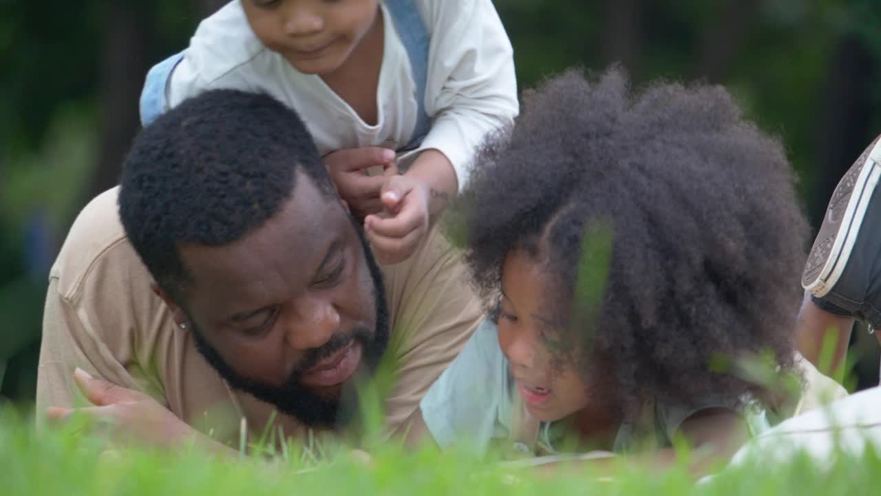 大流行期间，四名非洲裔家庭成员带着4-5岁的小男孩和小女孩一起躺在露天课堂的草地上。野餐的概念。视频素材