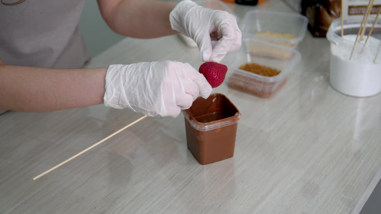 一个戴着白手套的女孩正在用牛奶巧克力准备草莓。视频下载