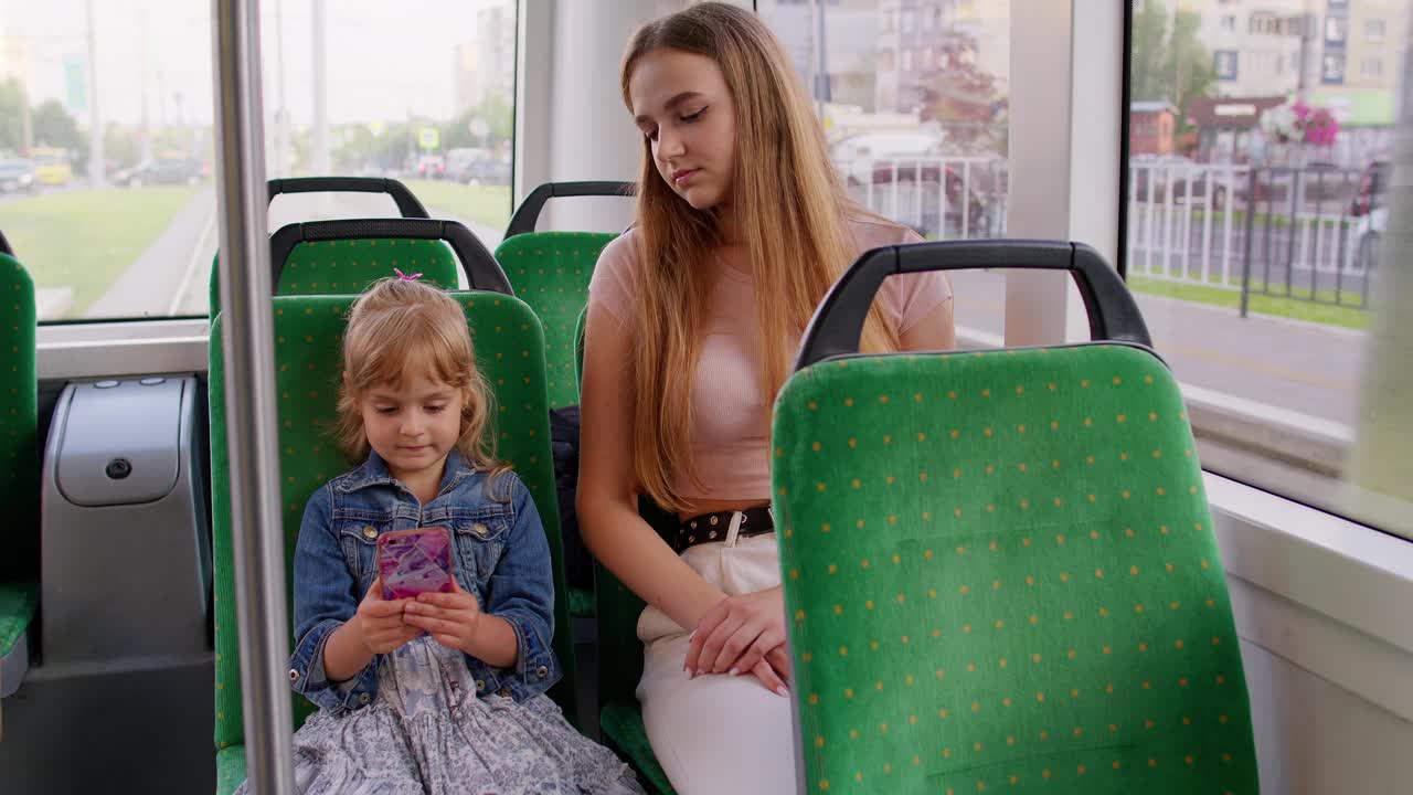 疲惫困倦的女人带着女儿在辛苦工作一天后坐公交车回家，孩子在玩智能手机视频素材