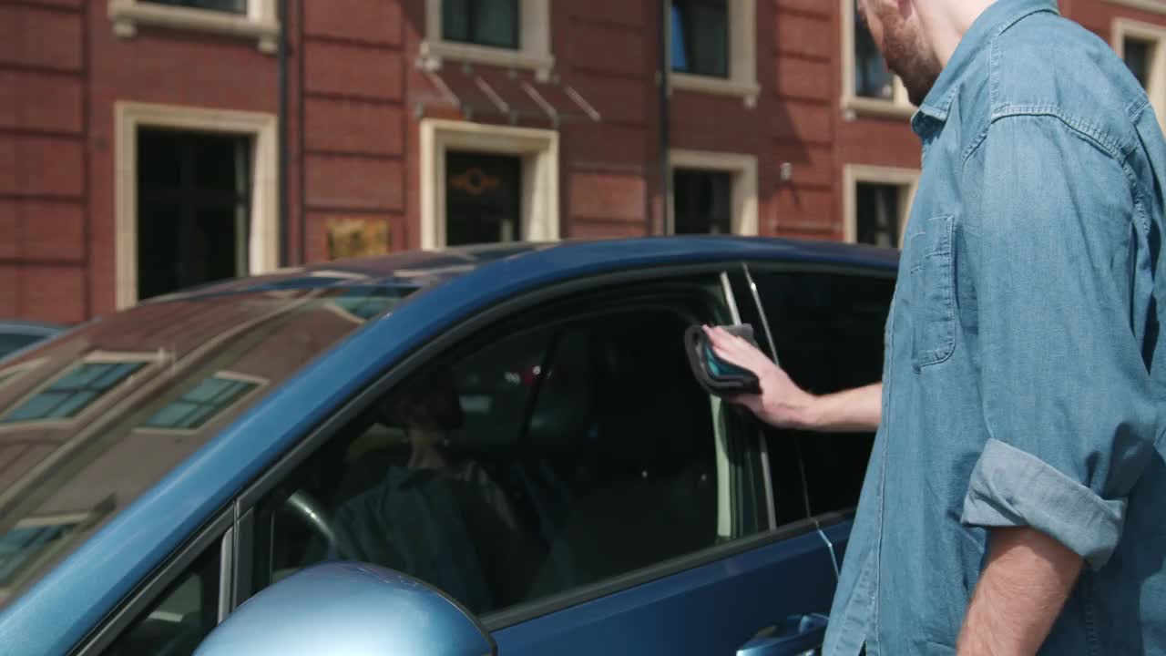一名身穿白色t恤和牛仔裤衬衫的司机正在清洗司机车门玻璃和侧镜视频下载