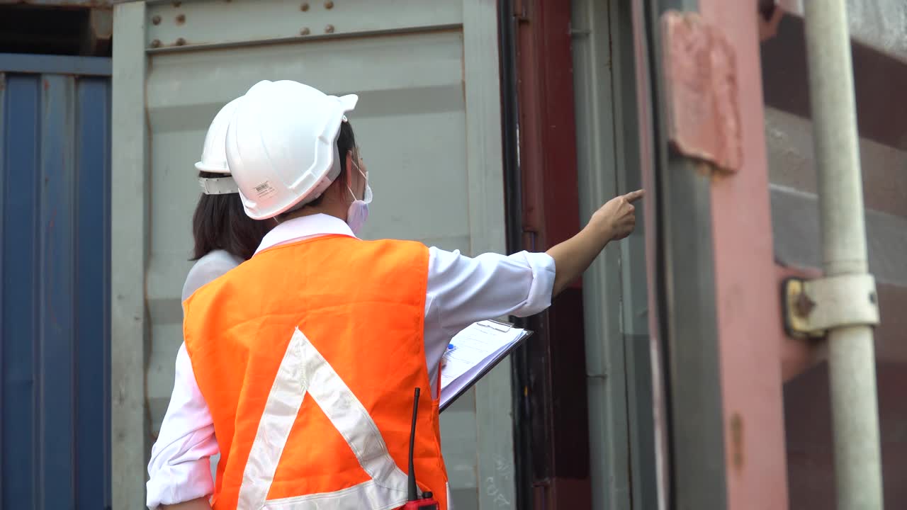 一群港务工作人员戴着口罩在货仓物流现场讨论并使用剪贴板检查集装箱箱内的质量。进出口运输业务的团队合作视频下载