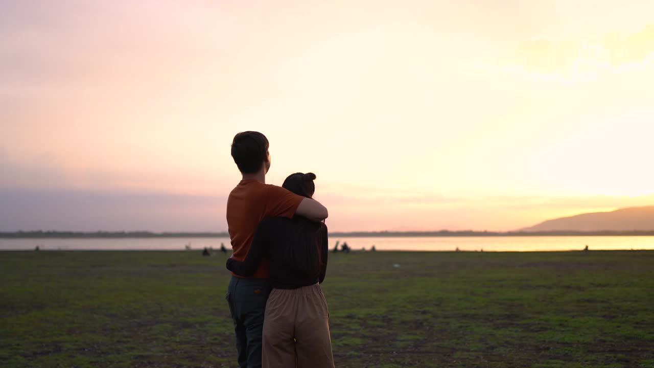 快乐和放松的年轻夫妇在绿色的田野在日落的背影。视频下载