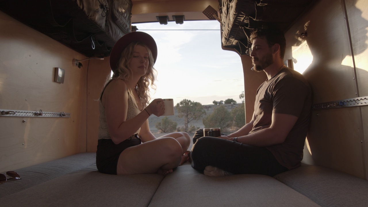 一对年轻的夫妇在他们的露营车里双腿交叉，在太阳落山的时候用他们的咖啡杯举杯庆祝视频下载