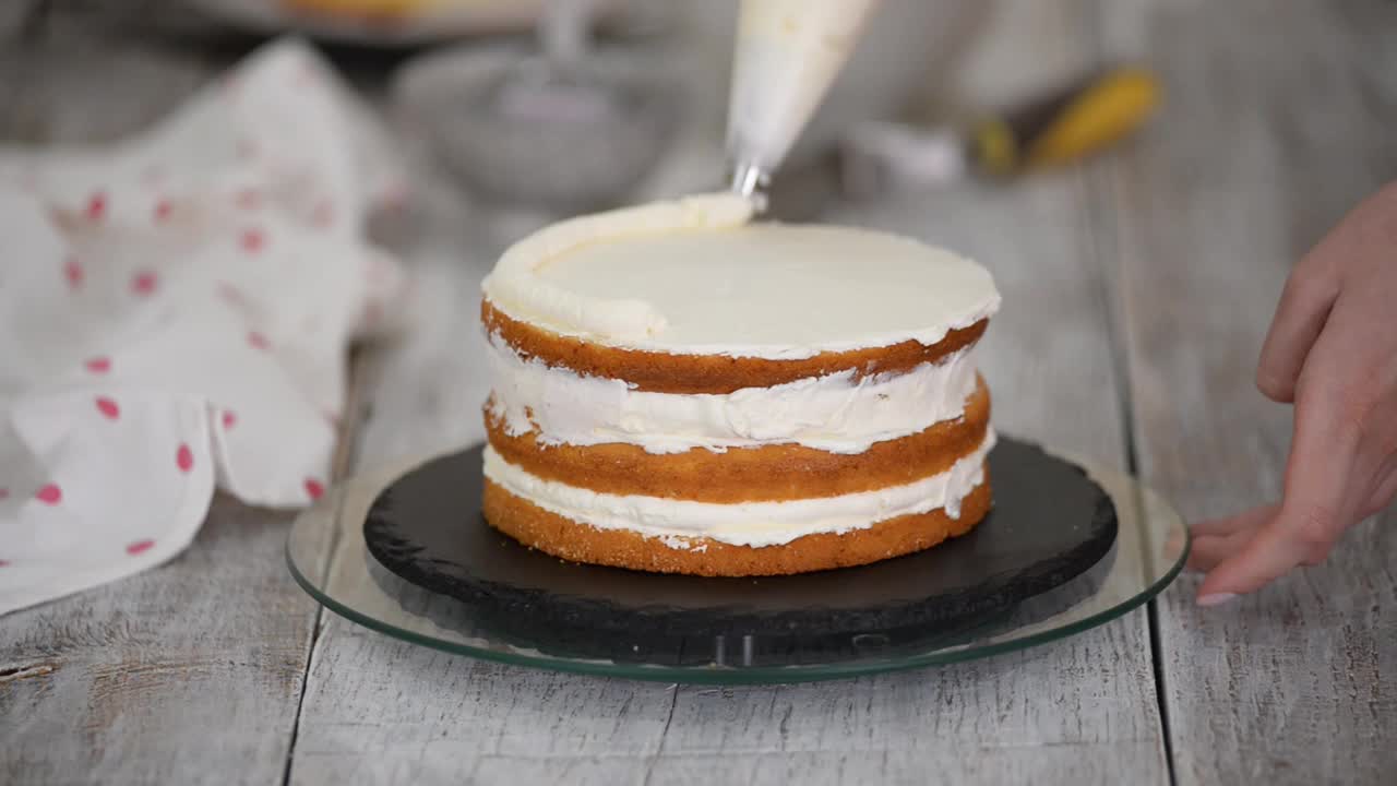 厨房里的糕点师用糕点袋在蛋糕上挤奶油。自制糕点的概念，烹饪蛋糕。视频下载