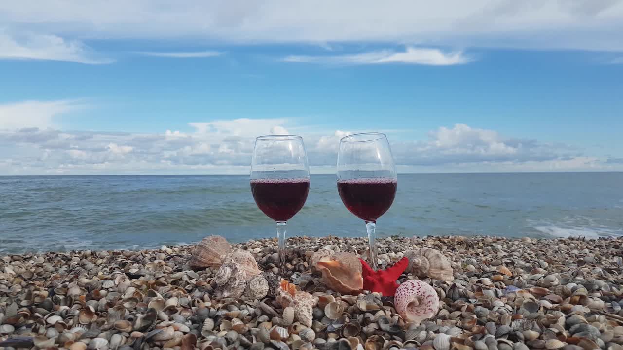 两杯盛满干红葡萄酒的杯子放在贝壳里，映衬着大海和蓝天白云视频素材
